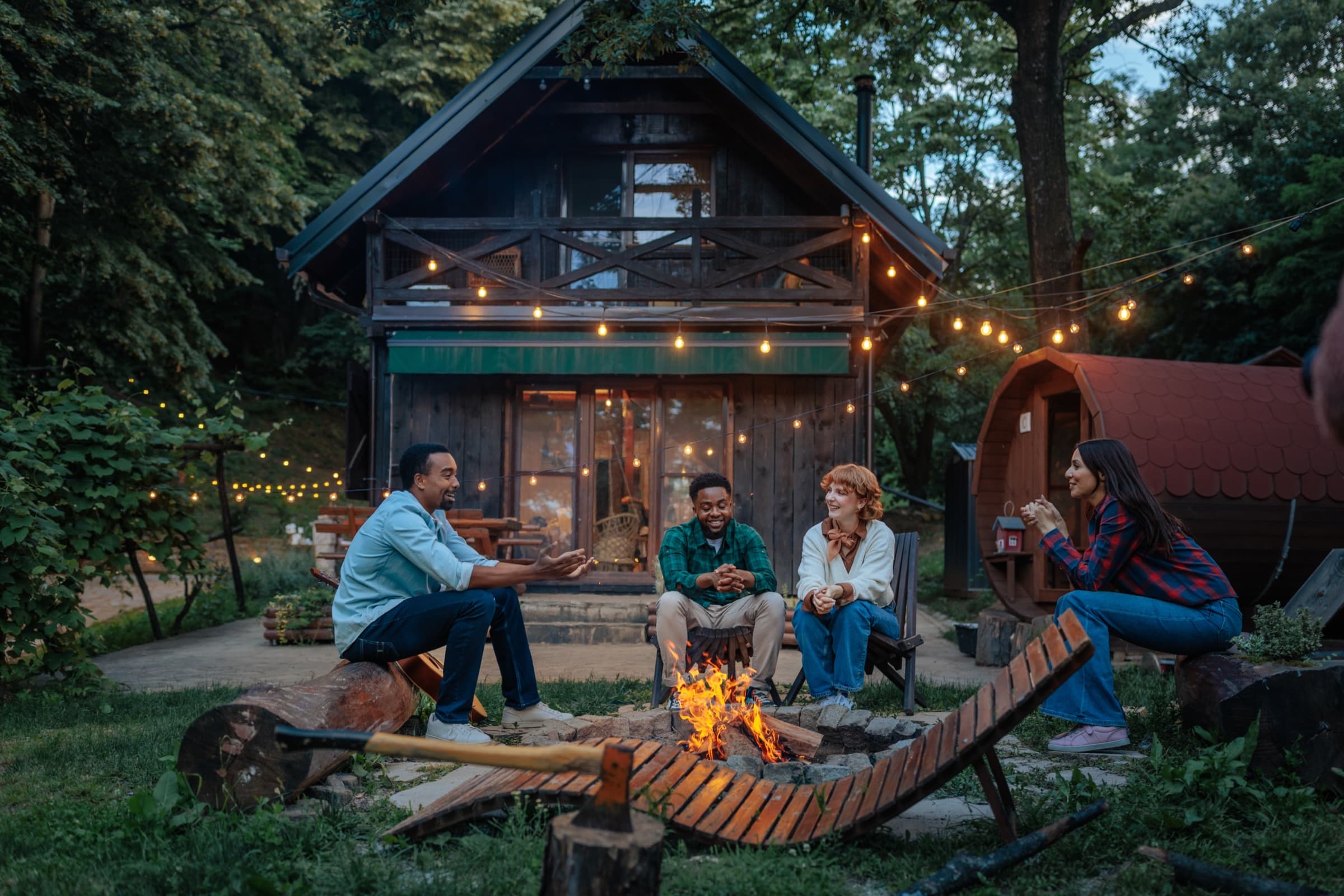 Friends gathered around a fire pit outside a cabin at dusk